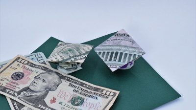 Dollar ORigami Graduation cap sitting on green paper with other dollar bills