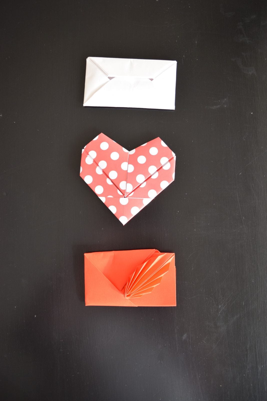 a white rectagular, polka dotted red and white heart shaped and a red with fan design valentine folded by origami