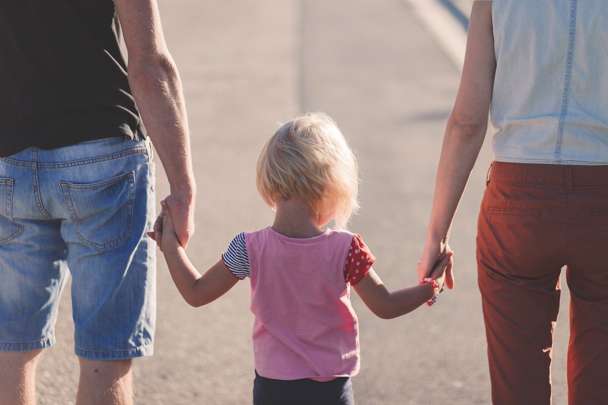 blonde girl walking away holding the hands of her parents