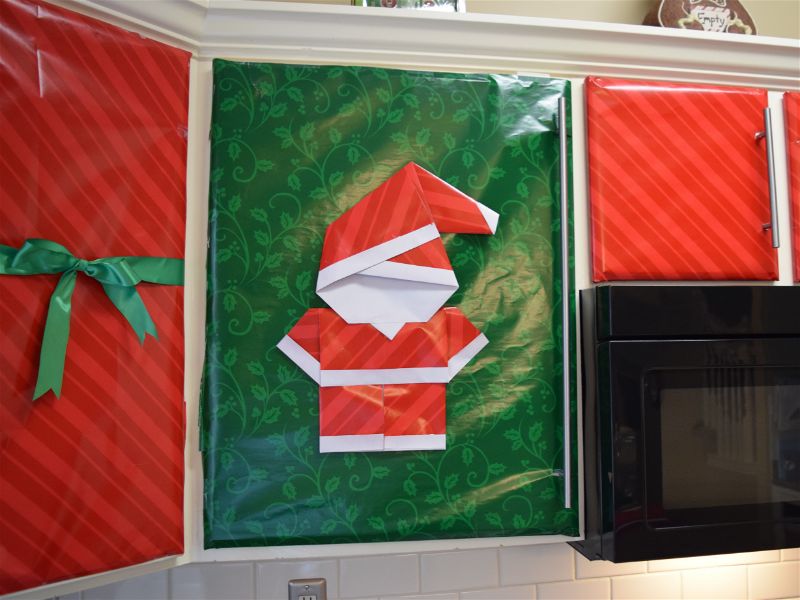 kitchen cupboards wrapped in red and green wrapping paper with a bow and a n origami santa decoration | FAvemom.com